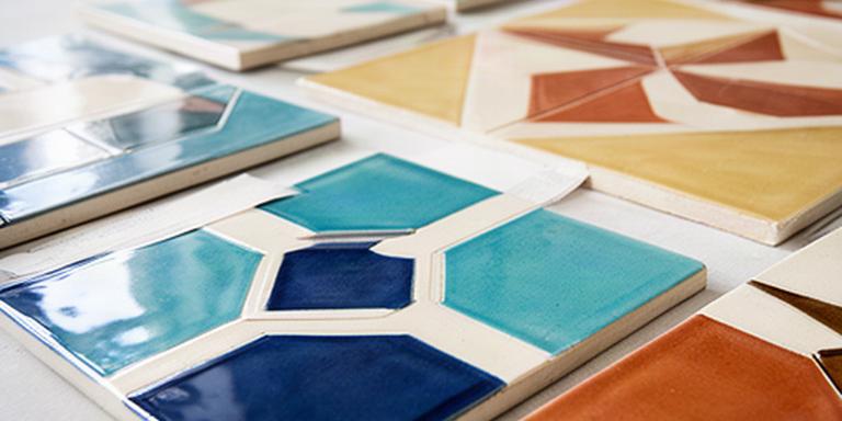 Piastrelle ceramiche smaltate con motivi geometrici esposte su un tavolo luminoso